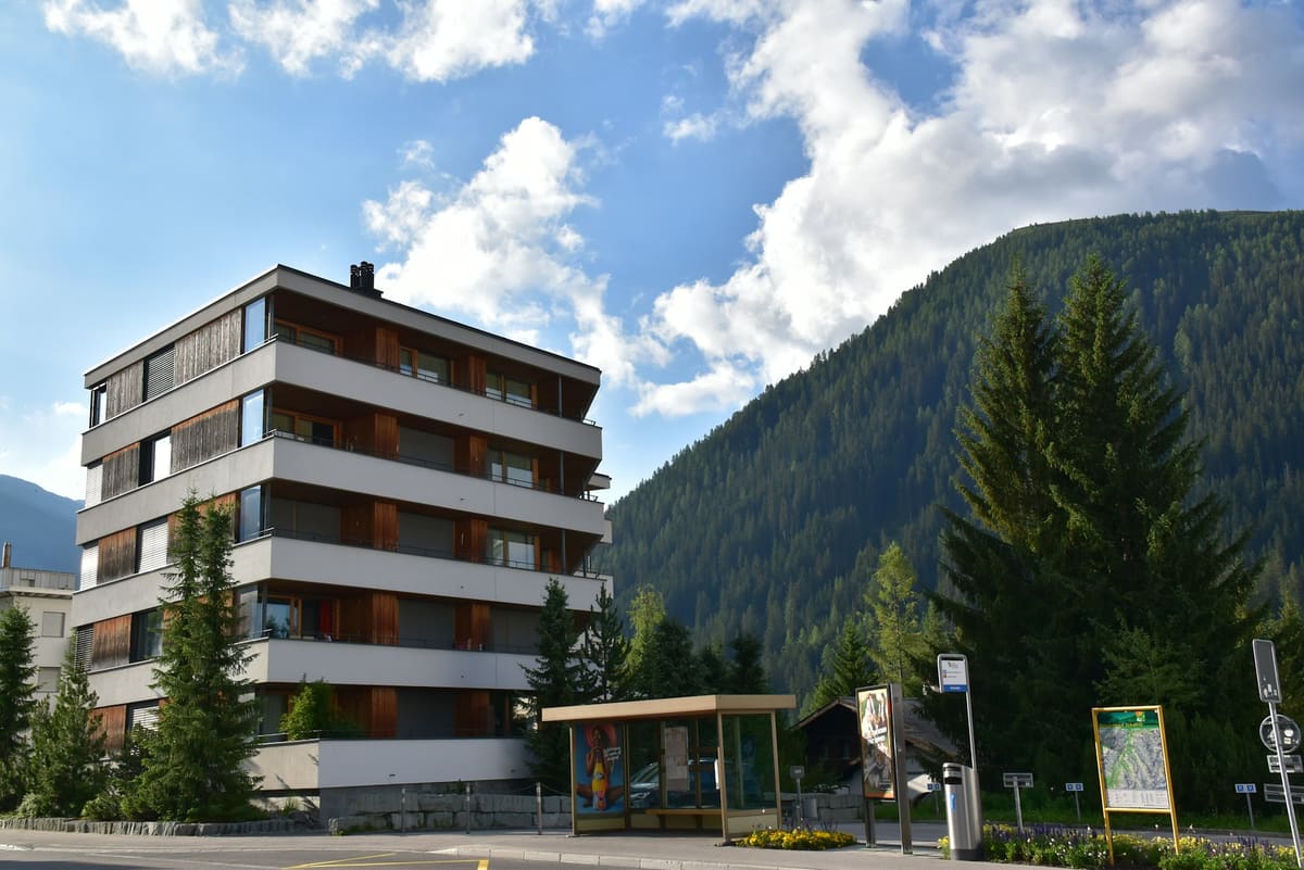 Modernes Mehrfamilienhaus mit Balkonen vor Bergkulisse