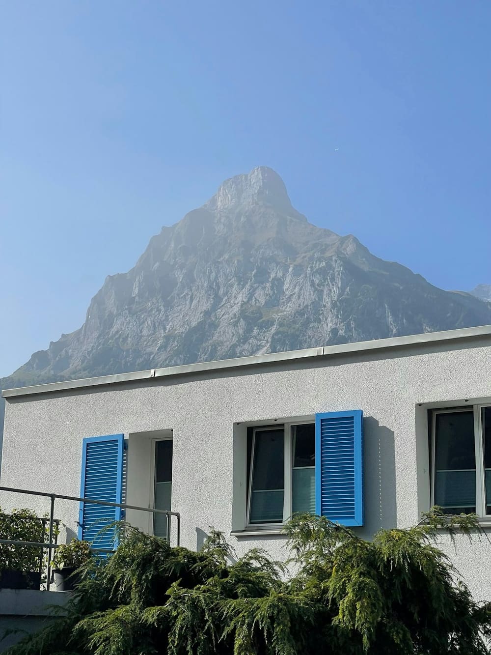 Wohnhaus mit blauen Fensterläden vor einem markanten Berggipfel